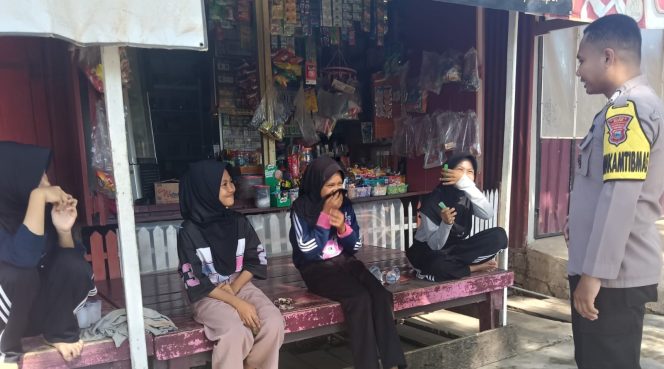 
 Bhabinkamtibmas Senyum Sapa Siswi Pelajar yang Asik Duduk di Depan Kios